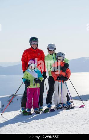 Una famiglia di quattro sorrisi con il lago Tahoe sullo sfondo mentre sciate presso la stazione sciistica di Alpine Meadows sulla riva nord del lago Tahoe, California. Foto Stock