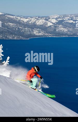 Una sciatrice (Hazel Birnbaum) scierà in neve profonda in una splendida giornata all'Heavenly Mountain Resort con il lago Tahoe sullo sfondo vicino al South Lake Tahoe, California. Foto Stock