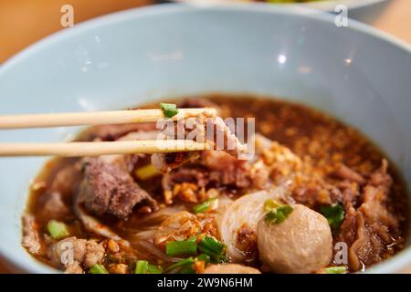 Raccogliete la carne brasata con le bacchette su spaghetti caldi in un recipiente Foto Stock