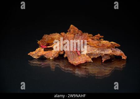 manciata di carne secca marinata con spezie, isolata su fondo nero. Spuntino con birra. Foto Stock