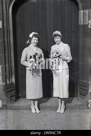 Anni '1950, storico, matrimonio, due belle ragazze, sorelle, sulla sinistra una sposa con la sua damigella d'onore all'ingresso della chiesa in piedi con mazzi di fiori, Inghilterra Regno Unito. Foto Stock