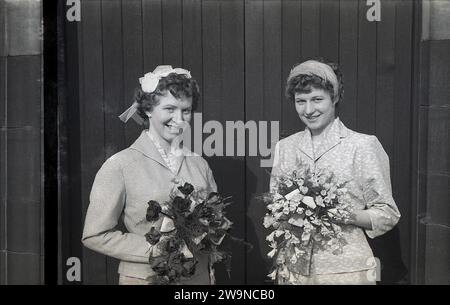 Anni '1950, storico, matrimonio, due belle ragazze, sorelle, sulla sinistra una sposa con la sua damigella d'onore all'ingresso della chiesa in piedi con mazzi di fiori, Inghilterra Regno Unito. Foto Stock