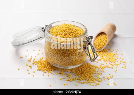 Seghetti di miglio in vaso di vetro e cucchiaio su un tavolo piastrellato bianco Foto Stock