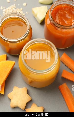 Barattoli con alimenti sani per bambini, zucca, carota e biscotti su sfondo grigio, sopra la vista Foto Stock