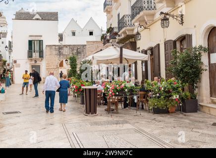 Locorotondo, Puglia, Italia - 5 ottobre 2023: I turisti si godono i ristoranti all'aperto nell'antico borgo di Locorotondo, in provincia di Bari. Foto Stock