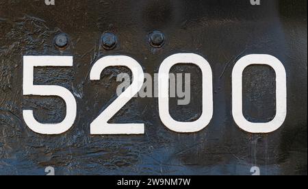 Numeri di agenti atmosferici zero, due, cinque, 5200 o 5, 2, 0 dipinto di bianco su un pezzo di metallo nero. Abstarct sfondo numerico per la progettazione. Foto Stock