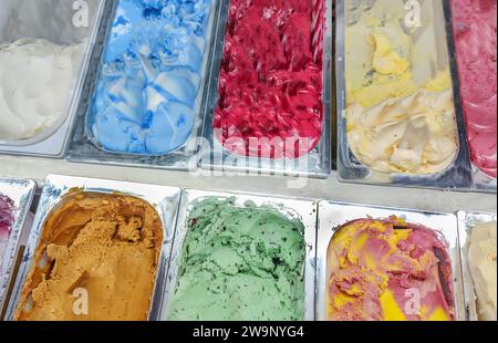 Ampia gamma di gelati di varie varietà e colori in contenitori di metallo sulla vetrina del negozio. Foto Stock