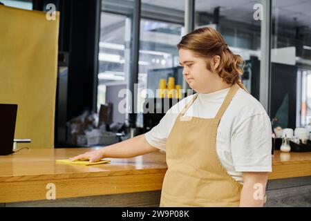 giovane dipendente donna con disturbi mentali che lavora in una caffetteria moderna e un bancone di pulizia con straccio Foto Stock