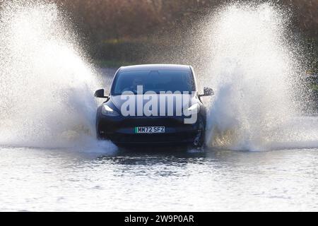 Un'auto elettrica che ha fatto un grande salto mentre viaggia attraverso una strada allagata a Fairburn, North Yorkshire, Regno Unito Foto Stock