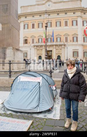 Roma, Italia. 29 dicembre 2023. LAURA FUNARO, 76 anni di Torino, ex dipendente dell'Ufficio postale italiano accanto alla sua tenda di fronte a Palazzo Montecitorio, sede della camera dei deputati della Repubblica Italiana, a Roma. Sulla tenda ci sono le frasi "lo sciopero della fame continua, lo sciopero della sete è rinviato per ora”. Laura protesta dal 17 ottobre perché sostiene di essere vittima di violazioni dei diritti costituzionali che hanno causato, tra l'altro, una riduzione dell'indennità pensionistica di circa 1/3 anni nonostante i suoi 48 anni di servizio. (Immagine di credito: © Mar Foto Stock