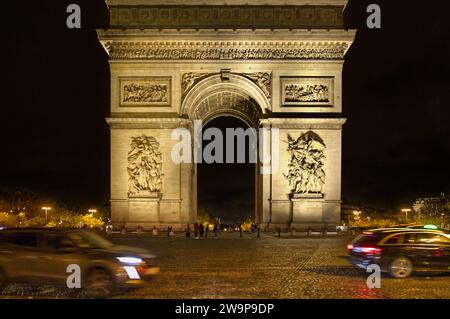 Place Charles de Gaulle o Place de l'Étoile, Parigi, Francia - Arco di Trionfo monumento con auto che lo circondano di notte Foto Stock