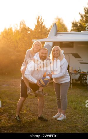 Genitori felici con il loro bambino che gioca con una palla vicino alla loro casa mobile nel bosco Foto Stock