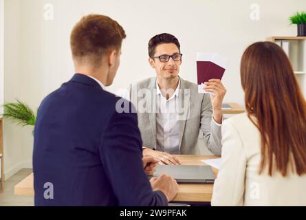 Coppia di famiglia seduta all'ufficio dell'agenzia di viaggi con un agente che dà loro passaporti con visto. Foto Stock