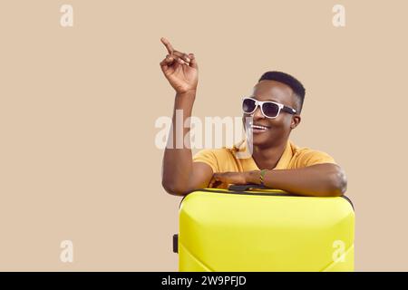 Felice turista afroamericano con occhiali da sole che puntano lateralmente su sfondo beige Foto Stock