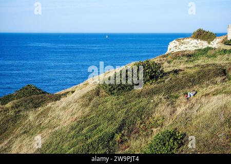 Una coppia amorevole che giace sul prato della scogliera a Sopelana, in Spagna, di fronte al mare al tramonto. Panorama incredibile e due abbraccianti sulla collina in estate. Foto Stock