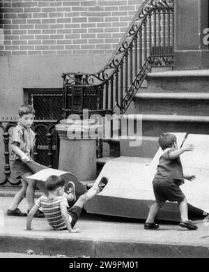 Tre ragazzi che usano il cartone per far scorrere i gradini di fronte all'edificio, New York City, New York, USA, Angelo Rizzuto, Anthony Angel Collection, agosto 1956 Foto Stock