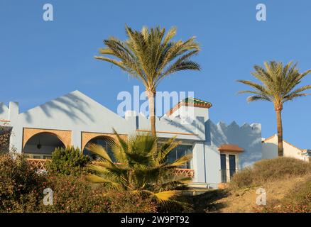 Bellissimo edificio spagnolo dipinto in terracotta e blu pallido con palme nel giardino Foto Stock