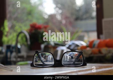 Un primo piano di un paio di occhiali neri su una superficie di legno all'interno di una cucina. Foto Stock