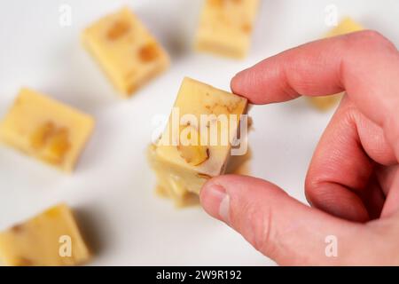 Turron natalizio spagnolo affettato su sfondo bianco. Mano che prende una singola fetta dolce da vicino Foto Stock