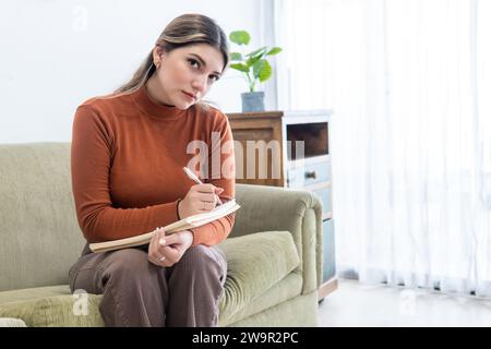 Giovane psicologo che guarda la macchina fotografica e prende appunti in una poltrona durante la terapia Foto Stock