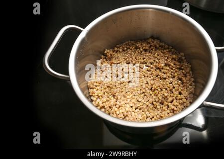 Cuocere il grano saraceno in una pentola d'acciaio sul piano cottura nero per un pasto sano e senza glutine, ricca fonte di proteine, fibre alimentari, quattro vitamine B e min Foto Stock