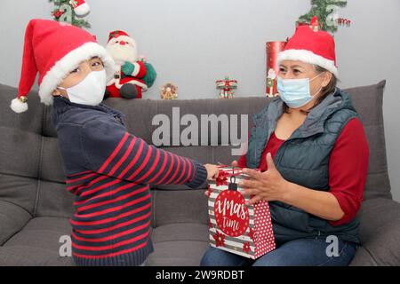 Nonna e bambino con maschera protettiva e cappello di babbo natale, regali e decorazioni natalizie, nuova covid-19 normale Foto Stock