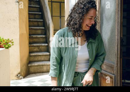 giovane donna venezuelana latina con i curler, che entra a casa sorridendo molto felice, in piedi a porta, spazio per copiare. concetto di stile di vita. Foto Stock