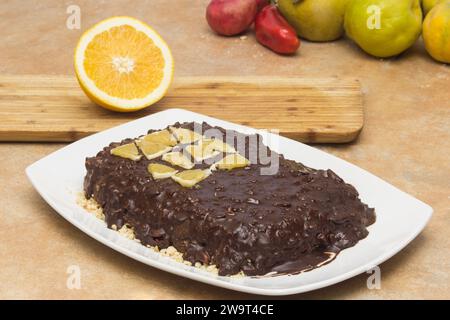 Un delizioso dessert al cioccolato con mandorle e frutta fresca, servito su un piatto bianco, in un ripiano rustico, circondato da frutta colorata. Fatti in casa o. Foto Stock