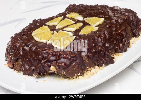 Una delizia fatta in casa al cioccolato e alle mandorle condita con fette d'arancia, posta su un piatto di ceramica bianca su un tavolo coperto da una tovaglia. cibo e ho Foto Stock