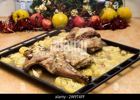 Un appetitoso agnello e patate appena arrostiti su un vassoio da forno, sullo sfondo di frutta fresca e decorazioni natalizie. Holida Foto Stock