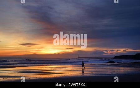 Un jogger corre all'alba lungo la spiaggia di Tynemouth, Tyne and Wear, sulla costa nord-orientale dell'Inghilterra. Durante l'ultimo fine settimana dell'anno sono in arrivo raffiche di neve come parte del brace britannico, sulle orme di pochi giorni ventosi dovuti a Storm Gerrit. Data immagine: Sabato 30 dicembre 2023. Foto Stock