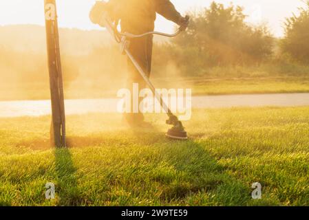 Un giardiniere con un rasaerba in mano taglia il prato all'alba. Foto Stock