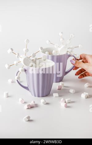 La mano di una donna che cerca la tazza. Tazze viola con marshmallow a fiocco di neve. Foto Stock