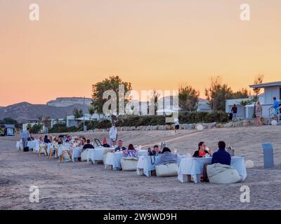 Gente che mangia all'aperto a Agios Stefanos Beach, al tramonto, isola di Kos, Dodecaneso, Grecia Foto Stock