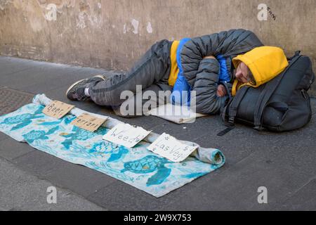 Roma, Italia. 30 dicembre 2023. Un uomo sta dormendo su un marciapiede e davanti a lui c'è un foglio dove i passanti lasciano alcune monete e piccoli segni con i suoi desideri: "Birra", "Ferrari", "erba", "Las Vegas" a Roma. Secondo il rapporto della Caritas sulla povertà e l'esclusione sociale in Italia, sono oltre 5 milioni 674 mila i poveri assoluti (un aumento di 357 mila persone rispetto al 2021), pari al 9,7% della popolazione: un residente su dieci oggi non ha accesso ad un dignitoso tenore di vita.secondo il rapporto, in Italia "chi nasce povero molto probabilmente lo farà Foto Stock