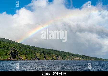 Un brillante arcobaleno si estende attraverso il cielo sopra le scogliere costiere del Parco Nazionale di Haleakalā, visto dall'autostrada Piilani a Maui. Foto Stock