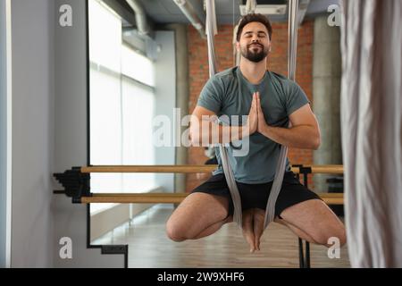 Giovane uomo che medita in un'amaca da yoga con la mosca al chiuso Foto Stock
