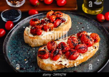 Toast al mascarpone con pomodori Burst: Fette di pane croccante condite con formaggio cremoso, pomodori d'uva carbonizzati e olio extravergine d'oliva Foto Stock