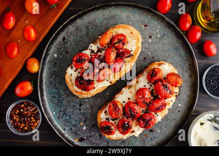 Toast al mascarpone con pomodori Burst: Fette di pane croccante condite con formaggio cremoso, pomodori d'uva carbonizzati e olio extravergine d'oliva Foto Stock