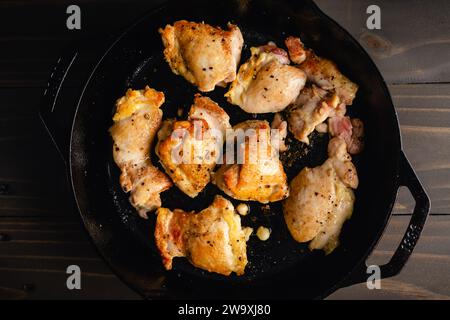 Cosce di pollo disossate e senza pelle in una padella di ghisa: Cosce di pollo scottate in padella condite con sale marino e pepe nero macinato fresco Foto Stock