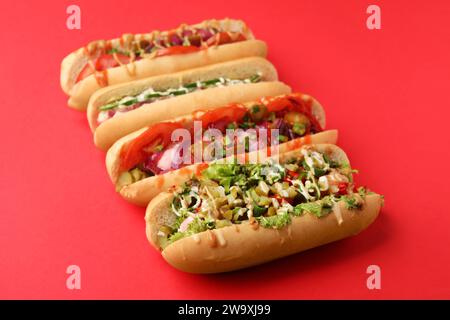 Deliziosi hot dog con diversi condimenti su sfondo rosso Foto Stock