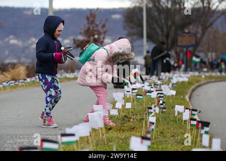 Harrisburg, Stati Uniti. 30 dicembre 2023. I bambini pongono piccole bandiere palestinesi nel terreno durante una manifestazione a favore della Palestina. I manifestanti hanno piazzato più di 20.000 bandiere, una per ogni persona uccisa a Gaza dall'inizio della guerra Israele-Hamas, lungo la strada vicino alla residenza del governatore della Pennsylvania. Credito: SOPA Images Limited/Alamy Live News Foto Stock