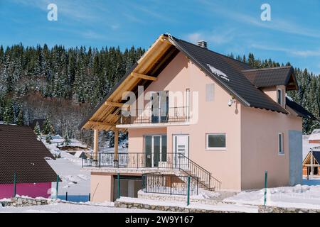 Casa rosa a due piani in un villaggio innevato ai margini di una foresta di conifere Foto Stock