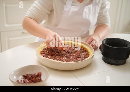 Una donna decora una torta rotonda con noci pecan. Processo di cottura della torta di noci pecan in cucina casereccia per il giorno del Ringraziamento americano. Foto Stock