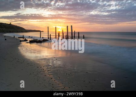 Le rovine del molo della spiaggia di Port Willunga nell'Australia meridionale si illuminano con il bagliore e i colori del tramonto. Foto Stock