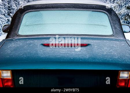 Vista posteriore ravvicinata di un'auto sportiva convertibile di colore verde scuro ricoperta di gelo e che passa davanti a alberi innevati Foto Stock