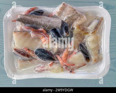 Pesce miscelato pulito e tagliato pronto per la cottura in pezzi congelati in vassoio sigillato sottovuoto su fondo di legno blu con percorso di ritaglio incluso, vista dall'alto Foto Stock