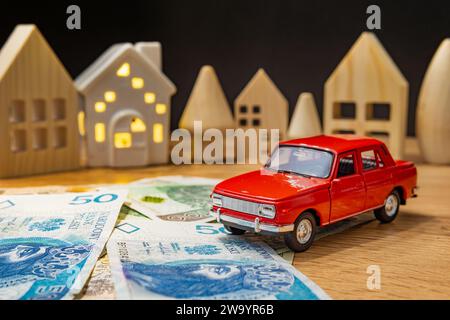 auto giocattolo con soldi polacchi e casa di legno che aumentano le spese per la vita crisi di inflazione tasso di interesse del prestito auto concetto Foto Stock