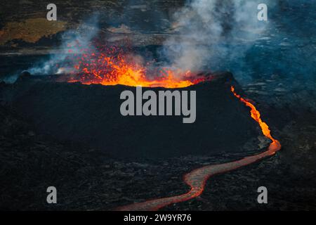 Eruzione vulcanica in Islanda, una fontana di lava rossa brillante che si innalza sopra uno sfiato e un flusso di lava che si diffonde rapidamente in discesa, colpo aereo. Foto Stock