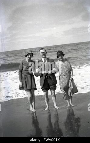 Anni '1950, storia, gente briitsh al mare..... in riva al mare, un uomo che indossa un abito e una cravatta, con i pantaloni arrotolati con due donne, vestiti e cappelli, che tiene le braccia. In questa e nelle epoche precedenti, le persone andavano al mare indossando abiti formali. Foto Stock